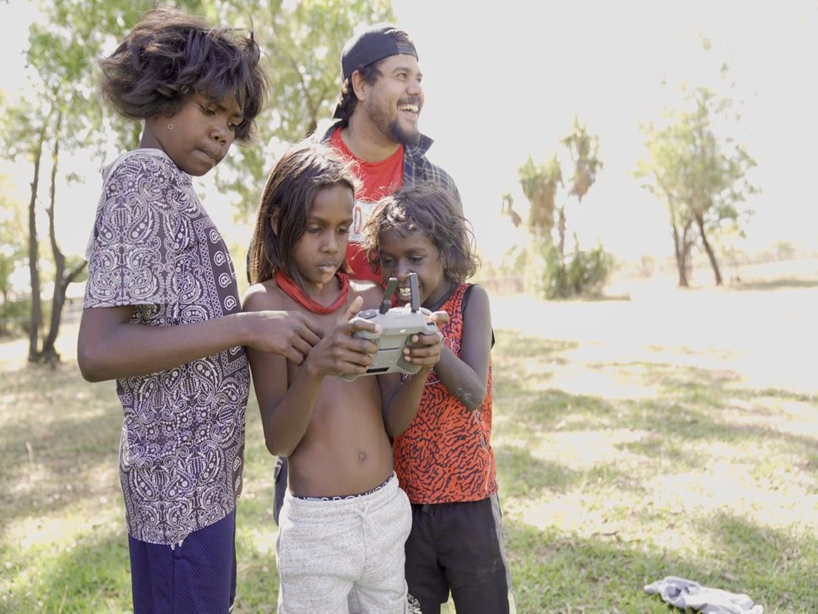 Three children playing on a remote-controlled device being supervised by an adult.
